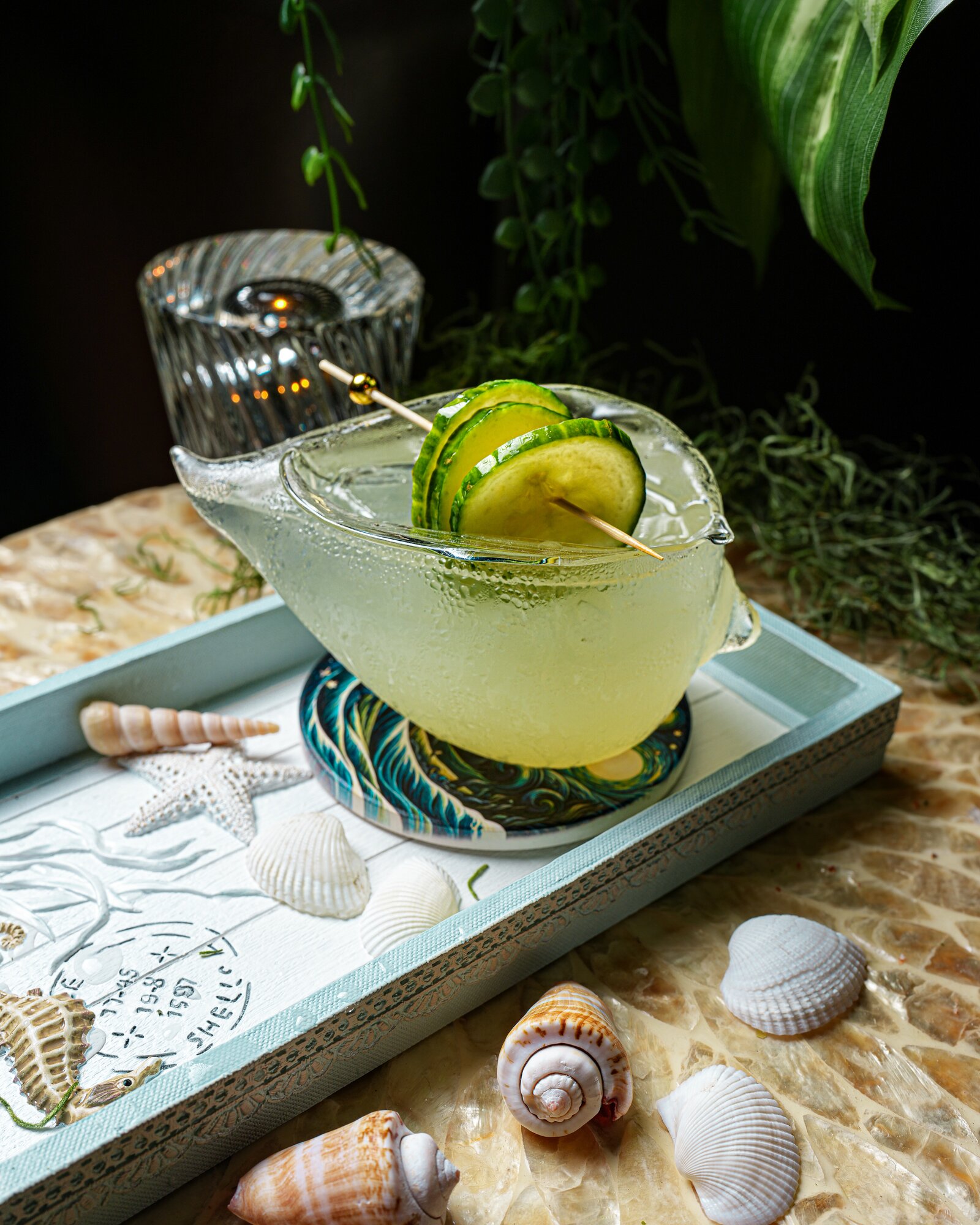 A cucumber cooler in a seashell glass on a coastal tray