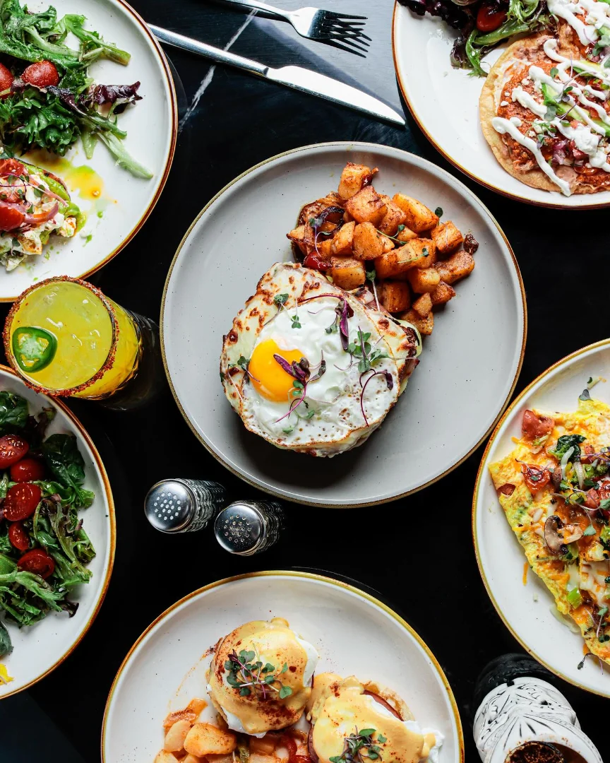 Overhead spread of Fuego brunch dishes — eggs benedict, omelets, salads and cocktails